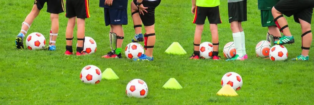 Kinder stehen beim Training zwischen Bällen und Hütchen