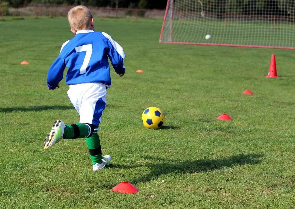 Kleiner Junge läuft beim Training zum Ball zwischen Hütchen